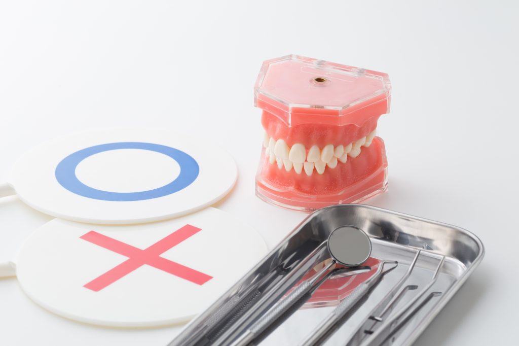 歯の模型と歯科治療器具とマルバツの札の写真